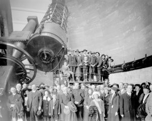 Photographie en noir et blanc d’un grand groupe de personnes devant un très grand télescope.