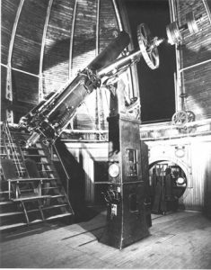 Image en noir et blanc d’une lunette astronomique de 15 pouces. Le télescope est fixé à un pilier de montage et se trouve à l’intérieur d’un bâtiment en forme de coupole. Une ouverture dans la coupole permet d’observer le ciel nocturne au moyen du télescope.