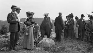 Photographie en noir et blanc de 1911 représentant un groupe de personnes au sommet d’une colline, debout et en train de discuter.