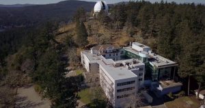 Photo prise par un drone d’un très grand bâtiment situé à flanc de colline. Au sommet de la colline se trouve une coupole de télescope blanche.