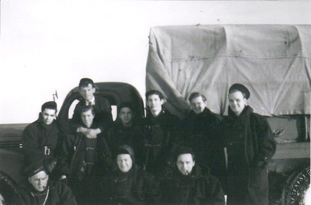 Photographie en noir et blanc de dix officiers de la Marine posant devant un camion couvert de la Marine.