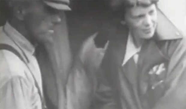 Amelia Earhart debout à côté de l’avion, en compagnie d’un homme inconnu avant le décollage.