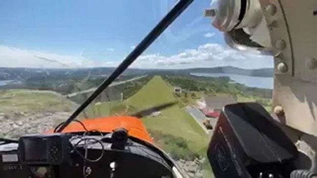 Photo en couleurs de l’intérieur d’un petit avion en vol pendant son approche pour atterrir sur une piste herbeuse.