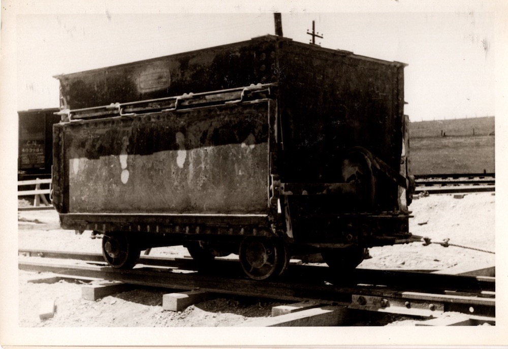 Photographie en noir et blanc d’un grand chariot métallique à quatre roues sur une chenille