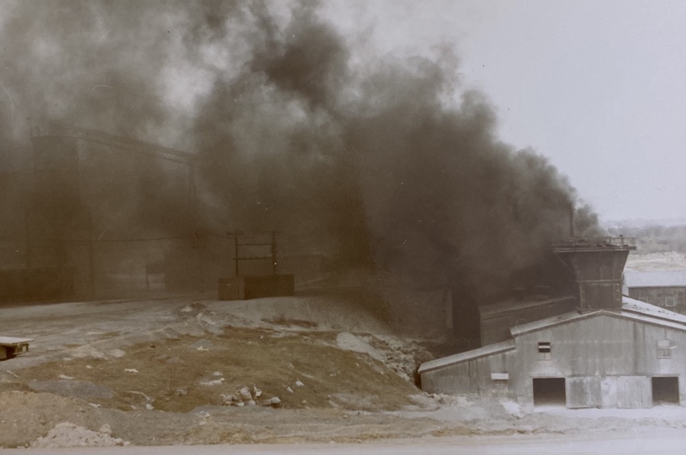 Un nuage de fumée noire s'élève d'un bâtiment industriel, masquant le paysage et les bâtiments au loin.