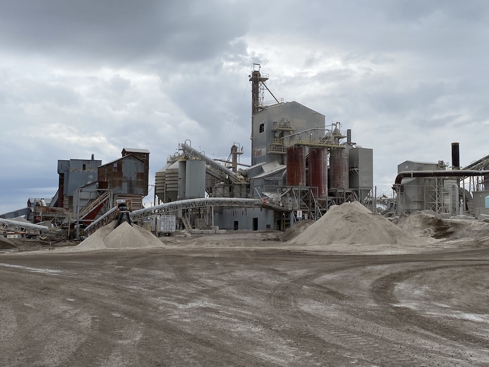 Une image en couleur de plusieurs bâtiments industriels, silos et tas de gravier sur un ciel nuageux