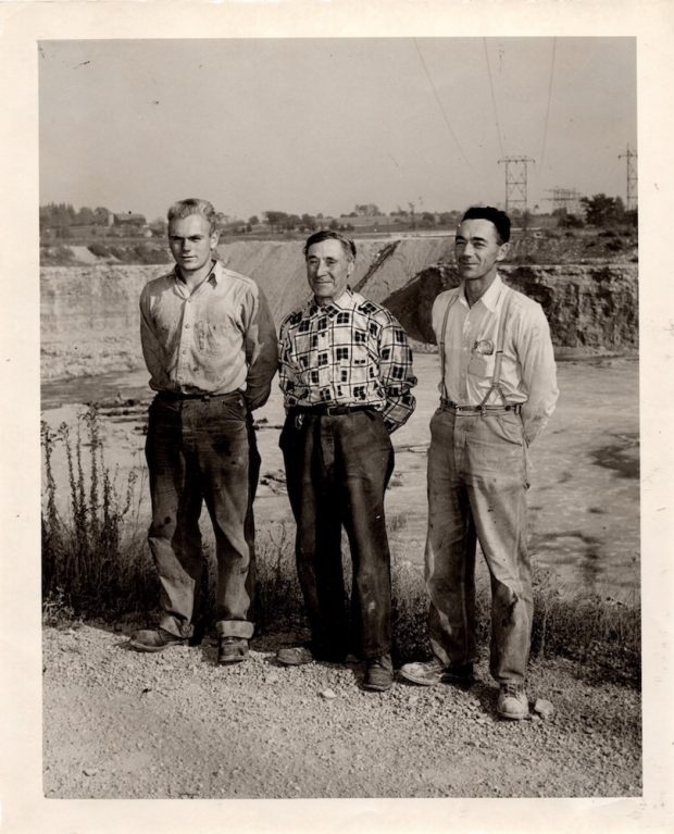  Photographie en noir et blanc de trois hommes debout ensemble au bord d’une carrière