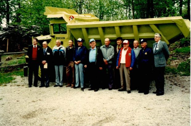 Un groupe de 12 hommes se tient devant un camion de transport de roches vertes