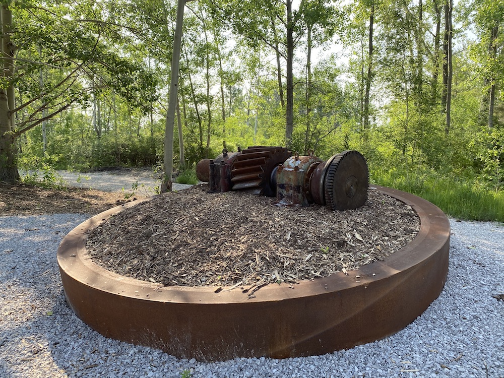 Image d'un engrenage rouillé posé sur un tas de paillis entouré d'une bordure métallique circulaire