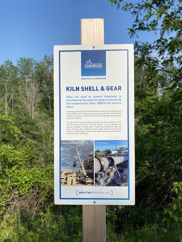 Un panneau sur un poteau en bois avec une bordure bleue, intitulé « Kiln Shell & Gear »