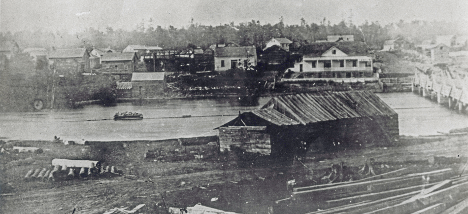 Photographie en noir et blanc d'un moulin à scie, vers 1850, avec le fleuve Mississippi et la ville d'Almonte en arrière-plan.