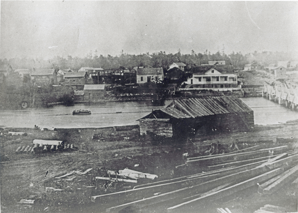 Photographie en noir et blanc d'un moulin à scie, vers 1850, avec le fleuve Mississippi et la ville d'Almonte en arrière-plan.