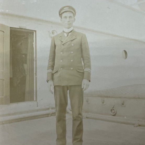 Photographie en sépia d'un jeune homme en uniforme debout sur le pont d'un navire.