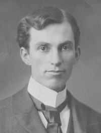 Portrait photographique en noir et blanc de John Francis Dunn, un jeune homme aux cheveux noirs portant une chemise blanche, une veste et une cravate.