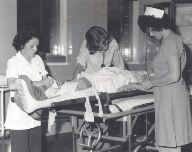 Photographie en noir et blanc de deux infirmières et d'un médecin avec un patient sur une civière.