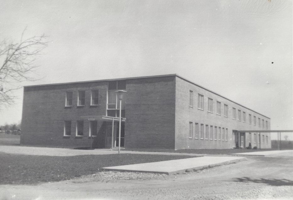 Photographie en noir et blanc d’un hôpital, un grand bâtiment en brique de deux étages.