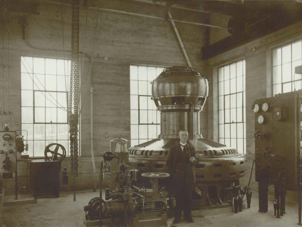 Photographie en noir et blanc d'un homme dans une grande pièce avec des machines.