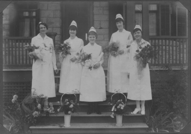 Photographie en noir et blanc de cinq femmes portant des uniformes d'infirmière et tenant des bouquets de fleurs.