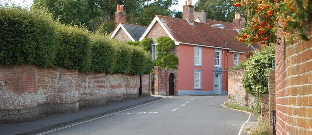 Photographie en couleurs montrant une maison rose sur une route sinueuse bordée d’un mur de briques.