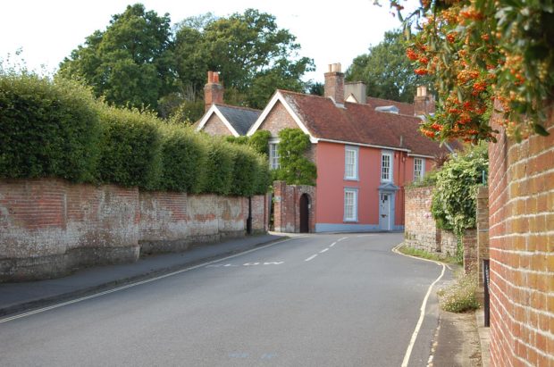 Photographie en couleurs montrant une maison rose sur une route sinueuse bordée d’un mur de briques.