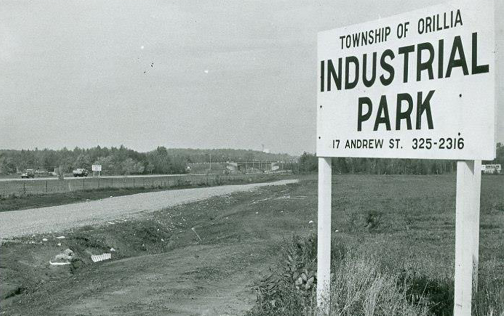 Photo en noir et blanc datant d’environ 1968. Un grand panneau blanc en bois dans la campagne affiche l’inscription en anglais : Canton d’Orillia, parc industriel, 17 Rue Andrew, 325-2316.