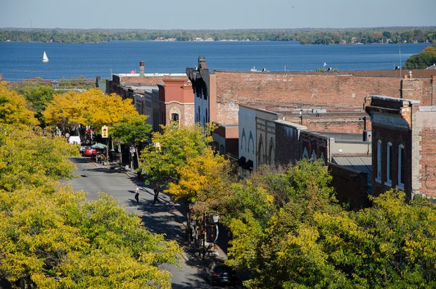 Vue du centre-ville d’Orillia surplombant des bâtiments historiques en brique rouge sur une rue bordée d’arbres. La surface du lac Couchiching apparaît au loin.