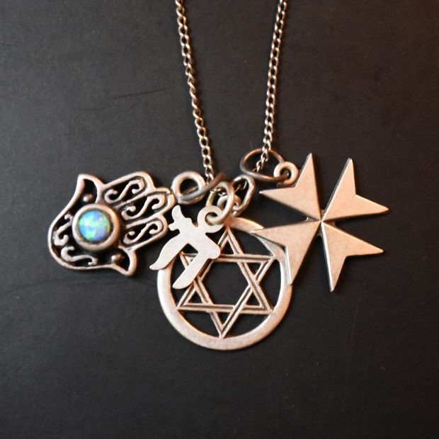 Quatre pendentifs sont accrochés à une chaînette en or : l’étoile de David, la croix de Malte, un caractère hébreu, et une main d'Harma sertie d’une pierre turquoise.