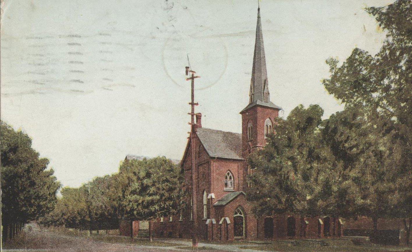 Carte postale colorisée d’une église orillienne sur une rue bordée d’arbres, vers 1909. L’église a un seul clocher et est faite en brique rouge.