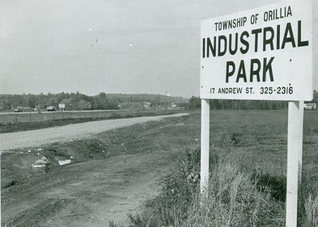 Photo en noir et blanc datant d’environ 1968. Un grand panneau blanc en bois dans la campagne affiche l’inscription en anglais : Canton d’Orillia, parc industriel, 17 Rue Andrew, 325-2316.