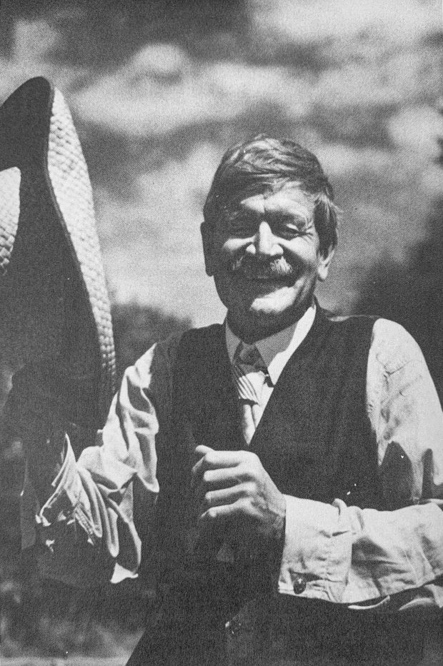 Portrait en noir et blanc de Stephen Leacock à l’extérieur, riant avec son chapeau de paille dans la main, vers 1941