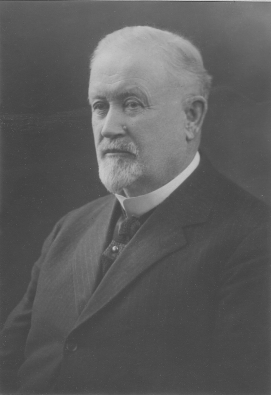 Photographie de studio d’un homme aux cheveux blanc qui porte un complet noir.