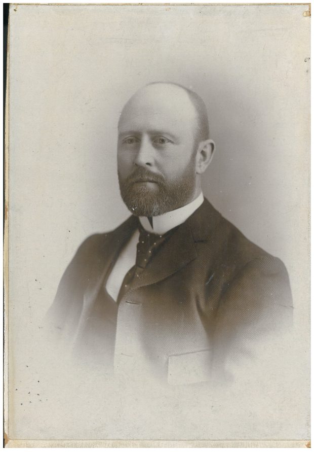 Photographie de studio d’un homme dans la quarantaine qui porte un complet noir et une chemise blanche.