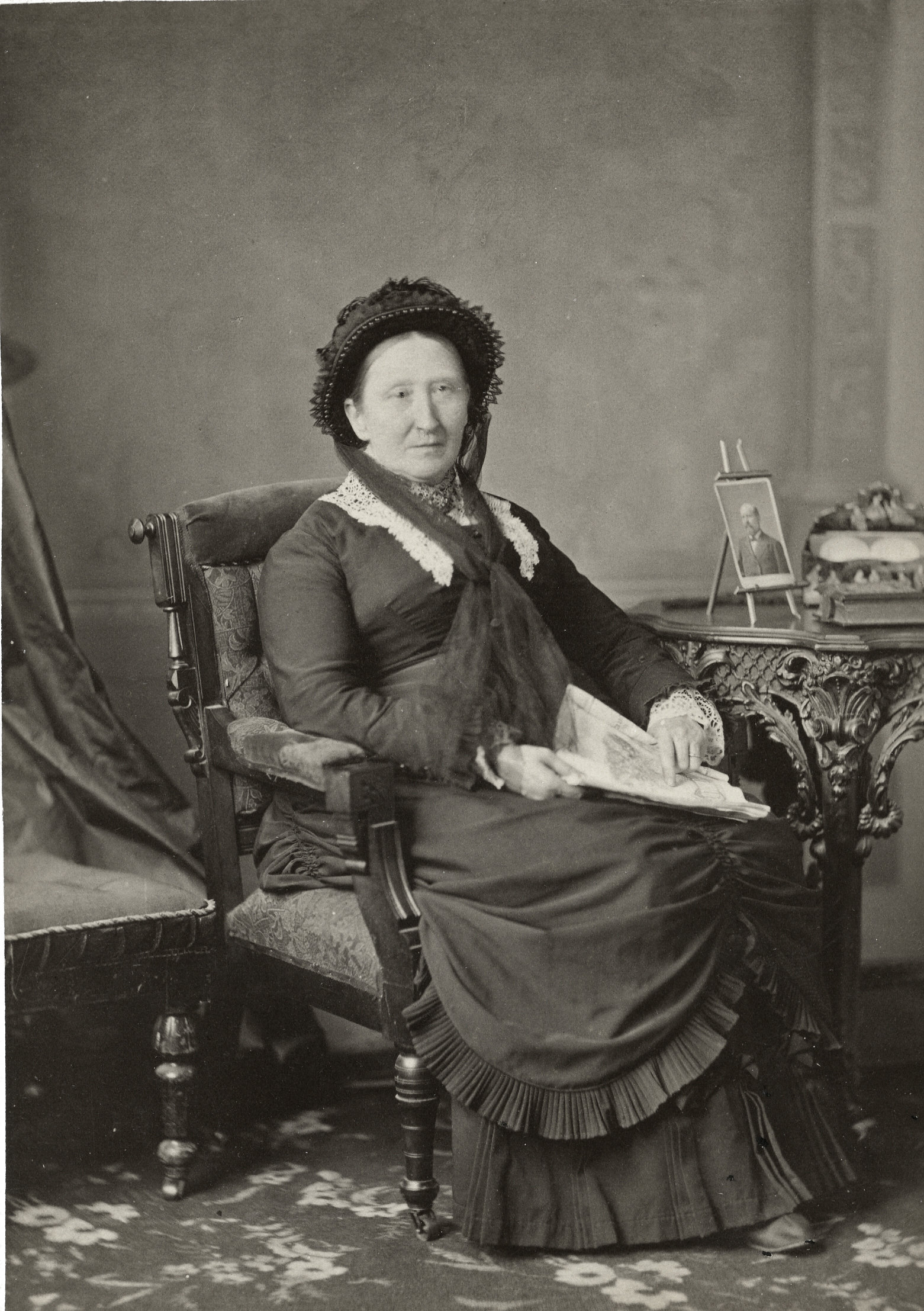 Photographie de studio d’une femme assise sur une chaise qui porte une robe noire.