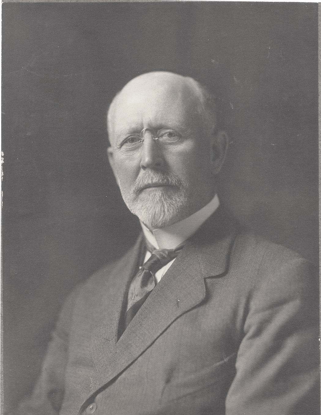 Photographie de studio d’un homme aux cheveux blancs qui porte un complet noir.