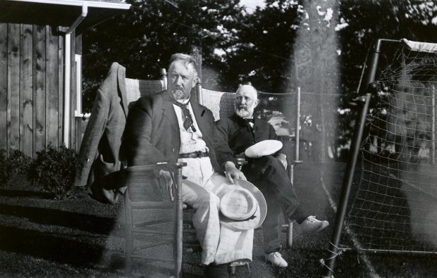 Deux hommes assis sur des chaises près d’un filet de tennis.