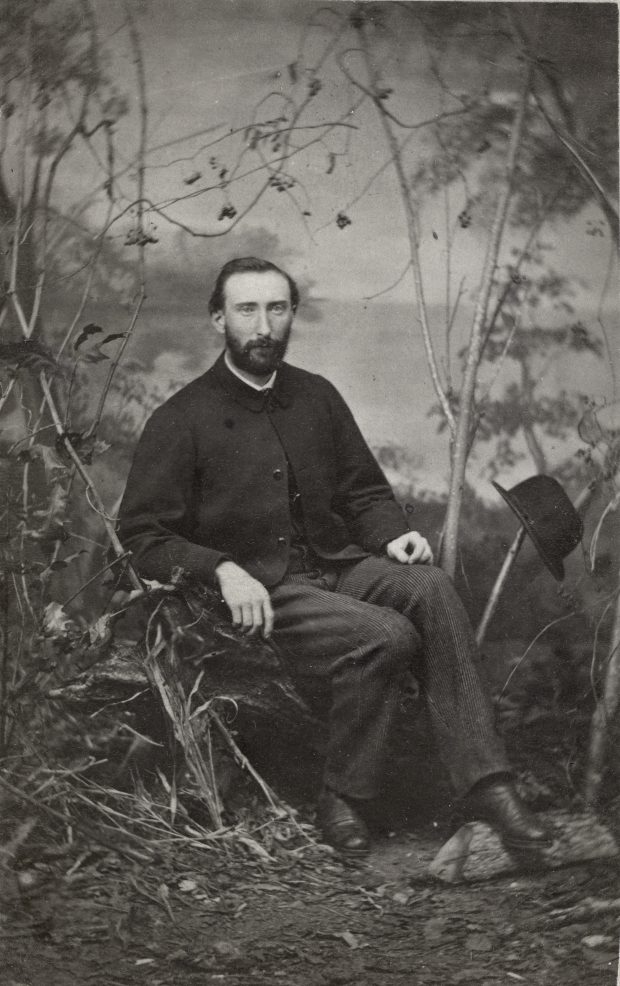  Photographie de studio d’un homme d’âge mûr assis près d’arbustes.