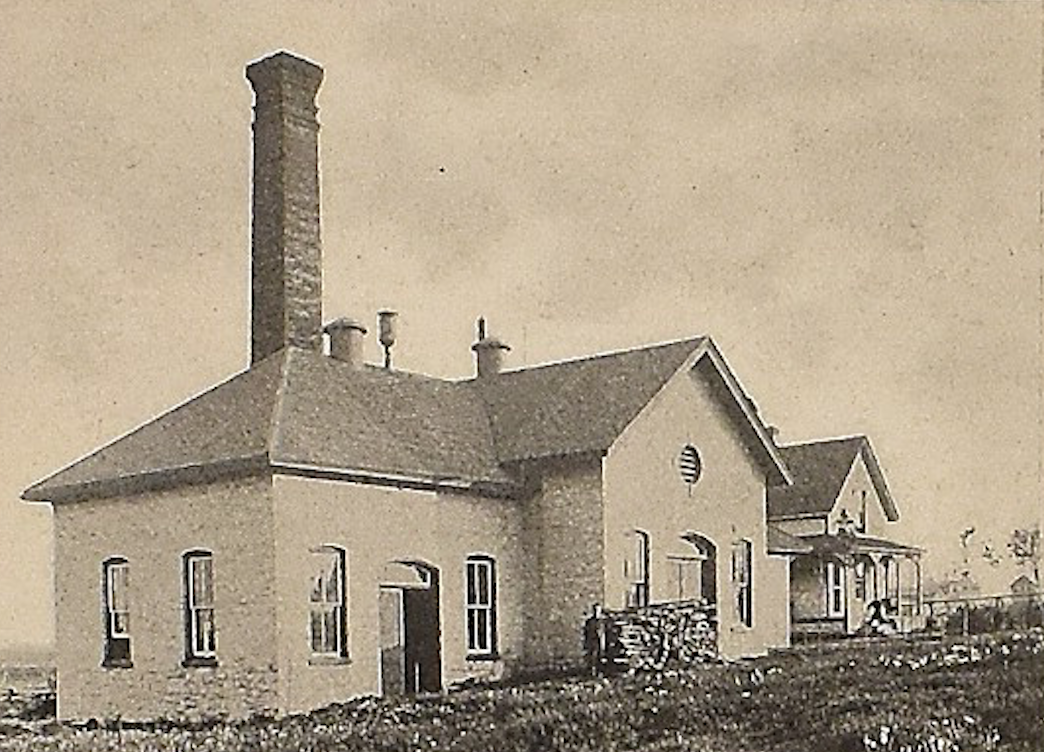 Bâtiment en briques muni d’une haute cheminée à l’arrière avec du bois coupé à l’avant-plan.