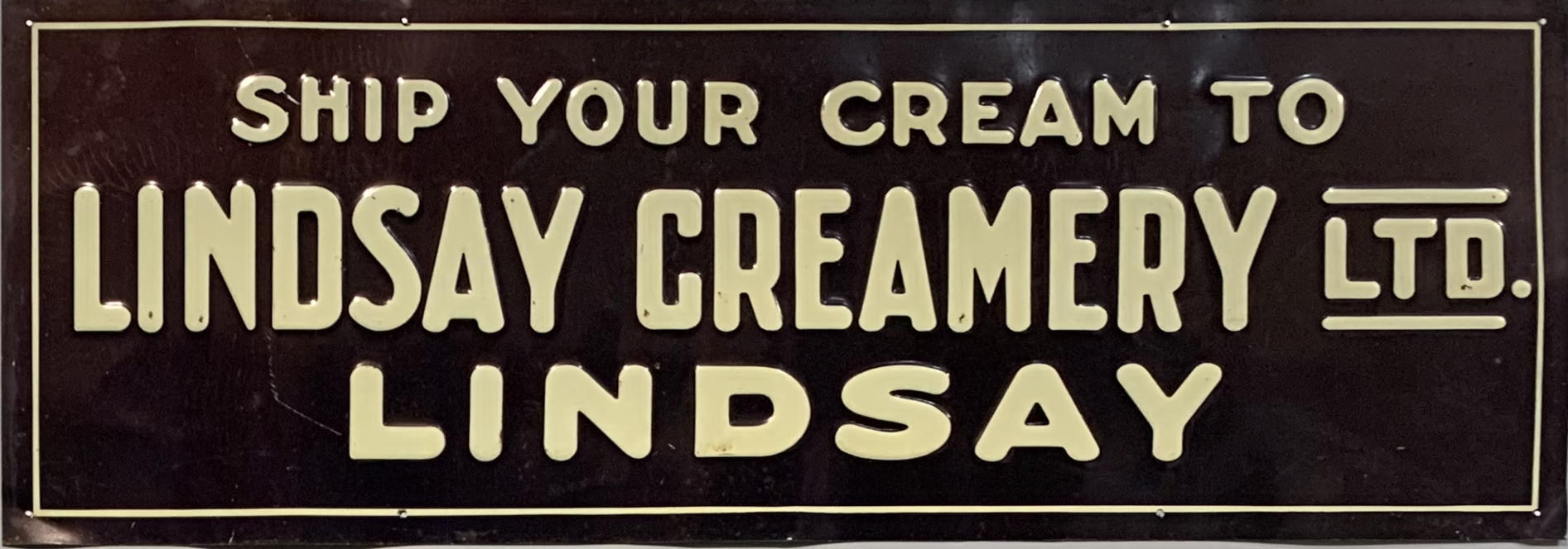 Affiche de métal peinte en noir et les mots Ship Your Cream To Lindsay Creamery Ltd. LINDSAY inscrits en lettres jaunes en caractères gras. 