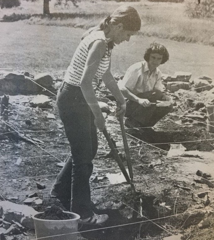 Photo en noir et blanc d'une femme debout tenant de longs ciseaux et jeune homme accroupi derrière, faisant des fouilles archéologiques dans un cadrilatère de corde.