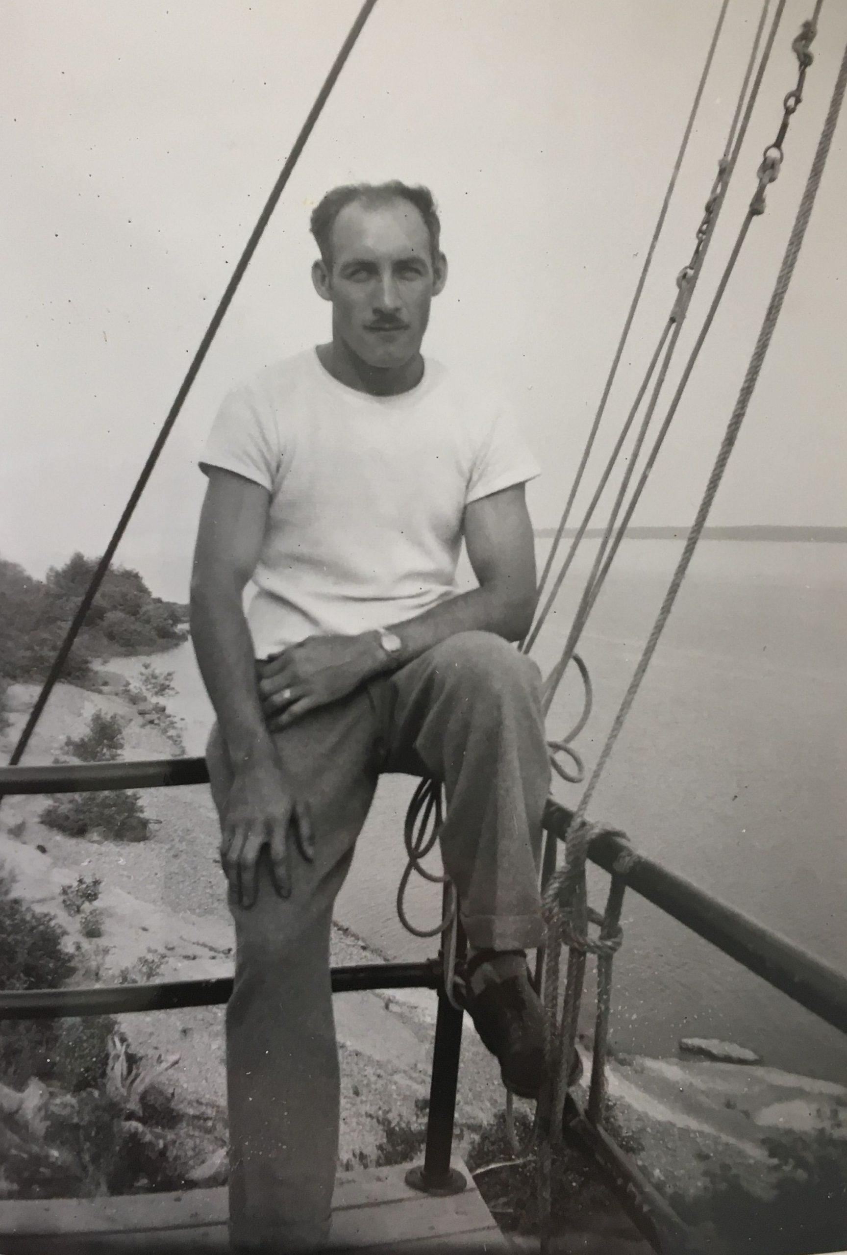 Photo en noir et blanc de Ovila Paquet assis sur la main courante d'un balcon. En arrière-plan, le fleuve. 