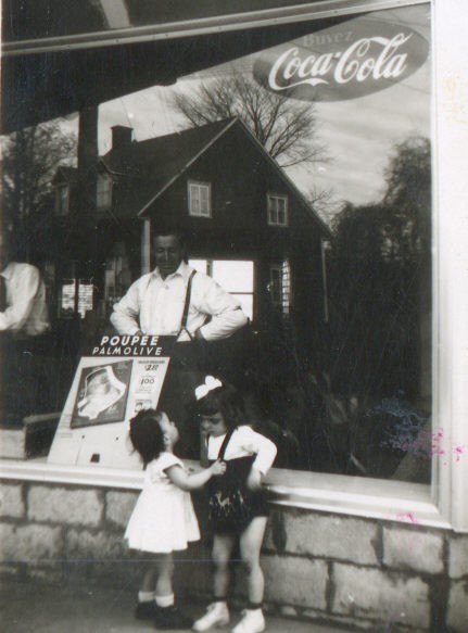 Photo en noir et blanc de deux enfants en bas âge devant une fenêtre avec un homme en arrière-plan.