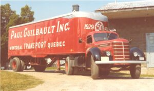 Photo d'un camion rouge sur lequel il est inscrit : « Paul Guilbault Inc. Montréal - Transport - Québec. 1929 - 50 - 1979 ».