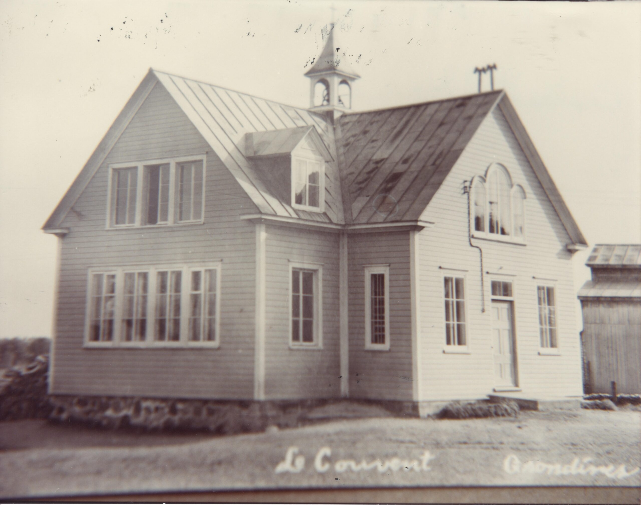 Photo en noir et blanc de l'école, un bâtiment deux étages surmonté d'un clocheton et à la partie centrale proéminente. 