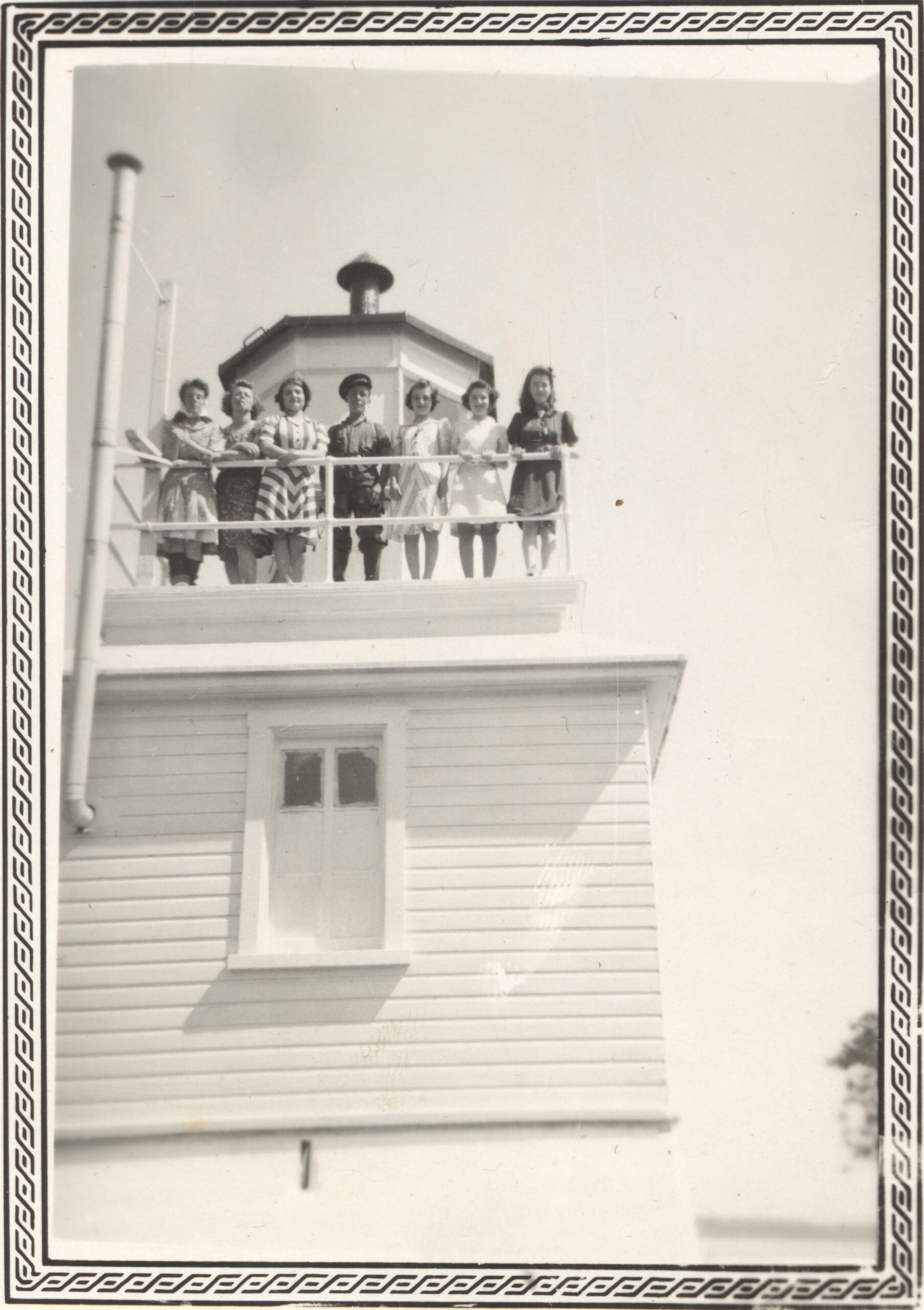 Photo en noir et blanc de six jeunes adultes en-haut d'un phare. 