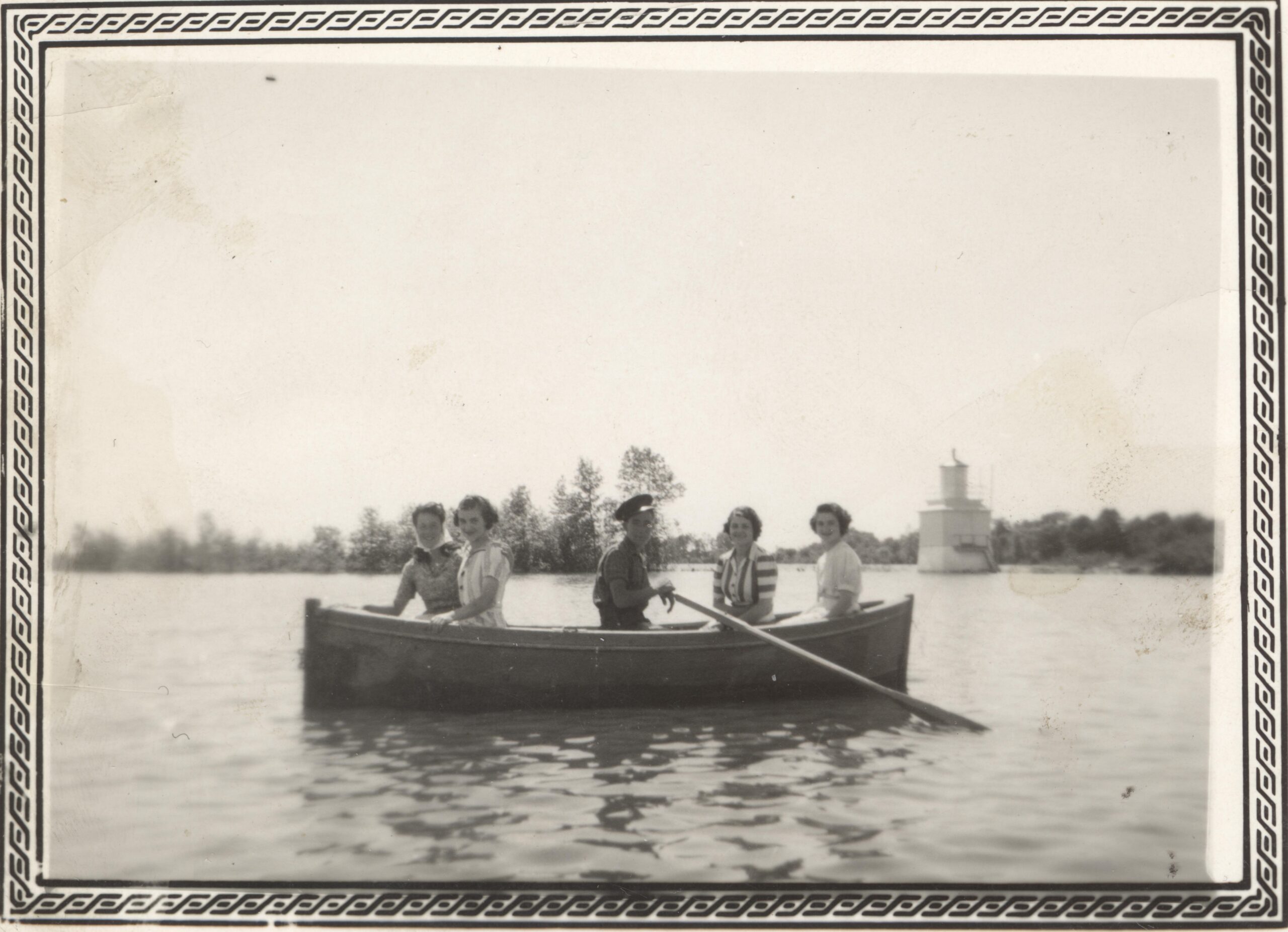 Photo en noir et blanc de cinq jeunes adultes en chaloupe. En arrière-plan, un petit phare dans l'eau. 