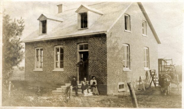 Photo noir et blanc de quatre personnes devant une maison de brique. 