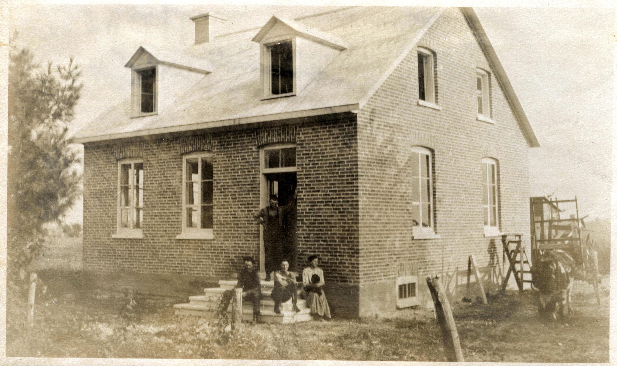 Photo noir et blanc de quatre personnes devant une maison de brique. 