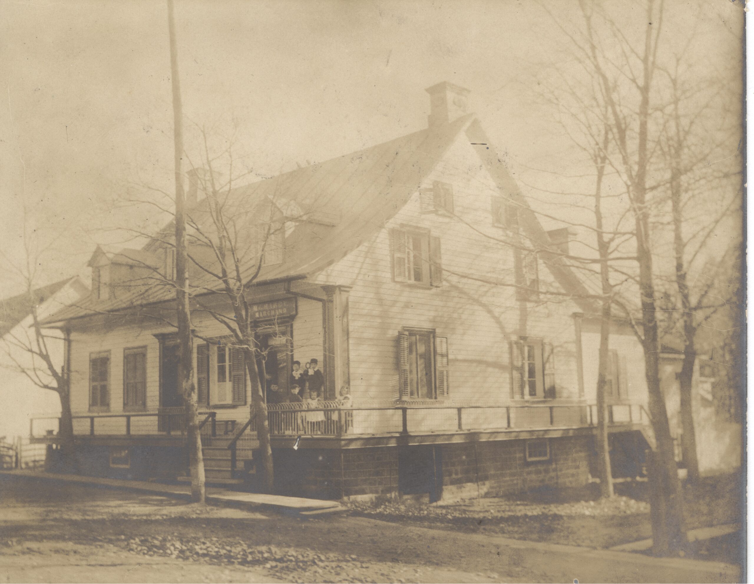 Photo en noir et blanc de six enfants sur la galerie d'une maison deux étages.