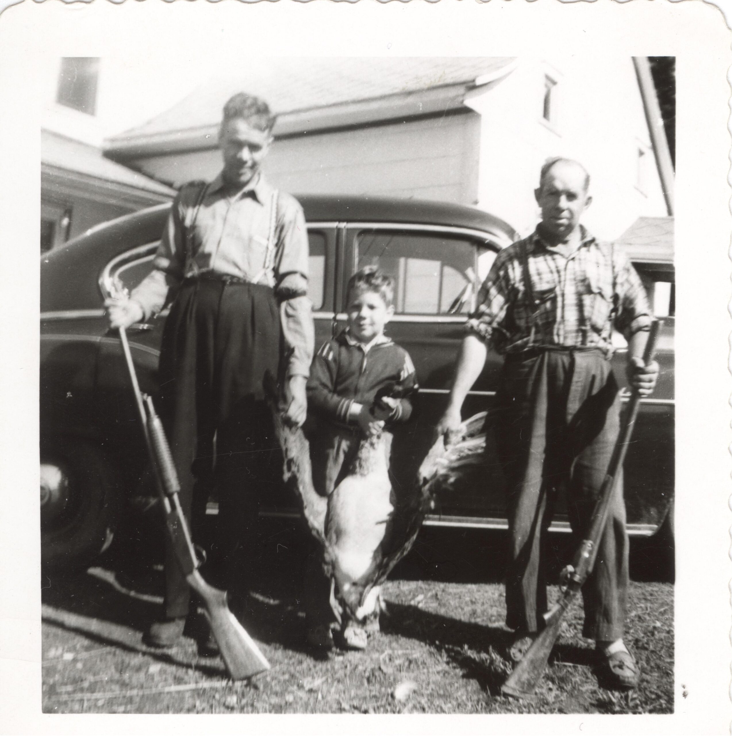 Photo en noir et blanc de deux hommes et un enfant tenant une outarde.