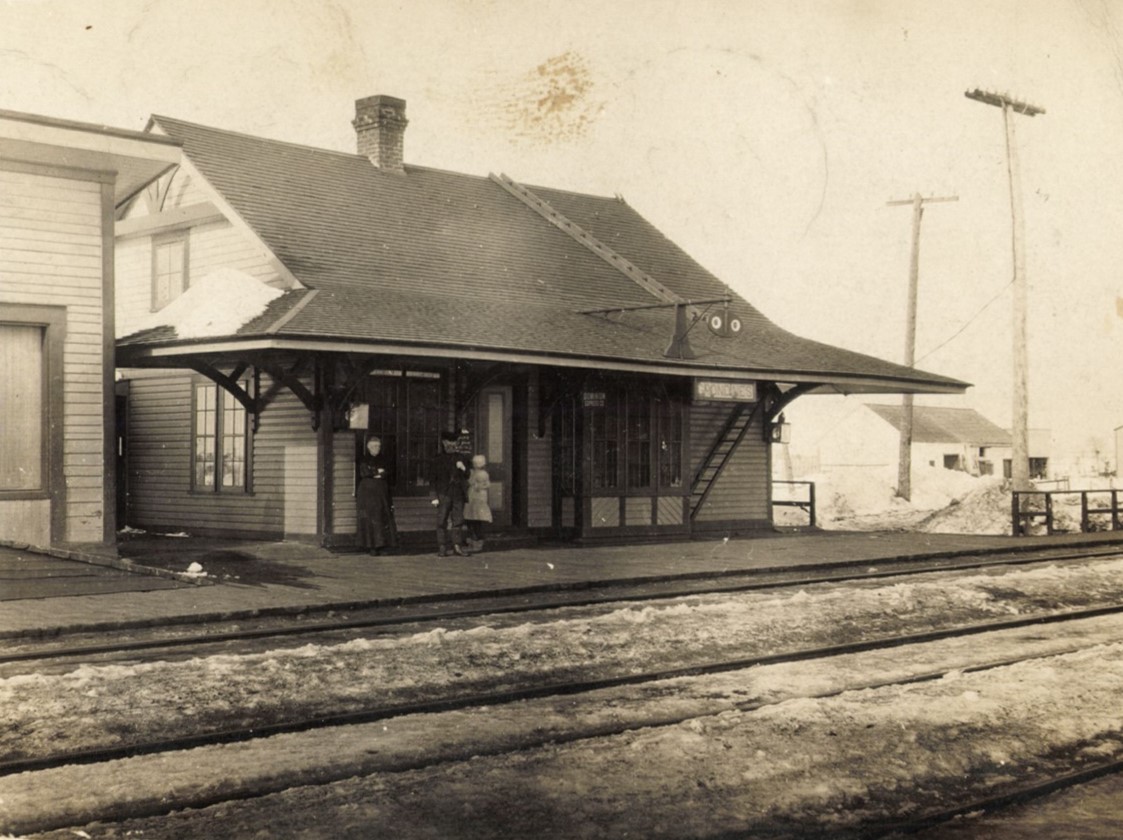 Photo en noir et blanc de trois personnes sur le quai de la gare de train en hiver.